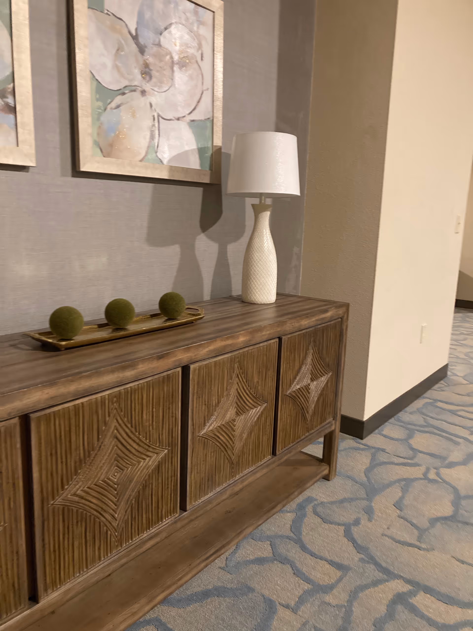 Wooden sideboard with a lamp and three moss balls in a patterned hallway.