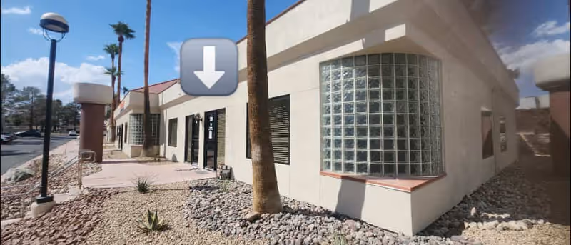 Exterior view of a beige building with glass block window, palm trees, and desert landscaping.