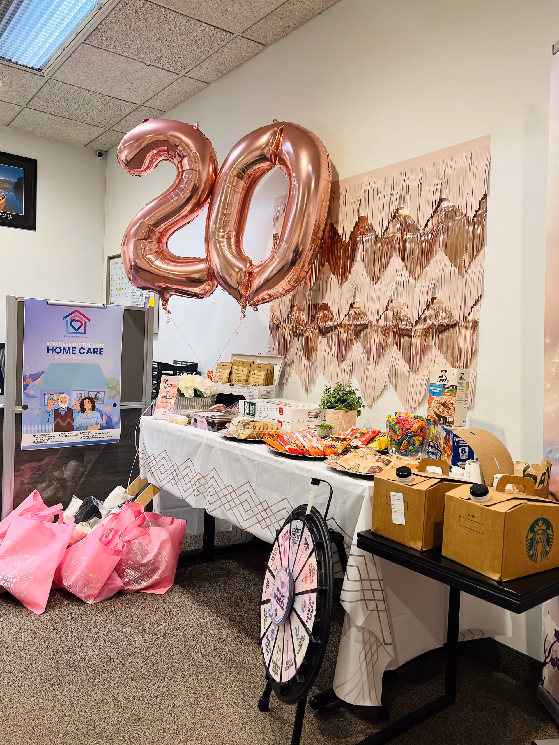 Indoor celebration area with large pink '20' balloons, a prize wheel, and a snack table.