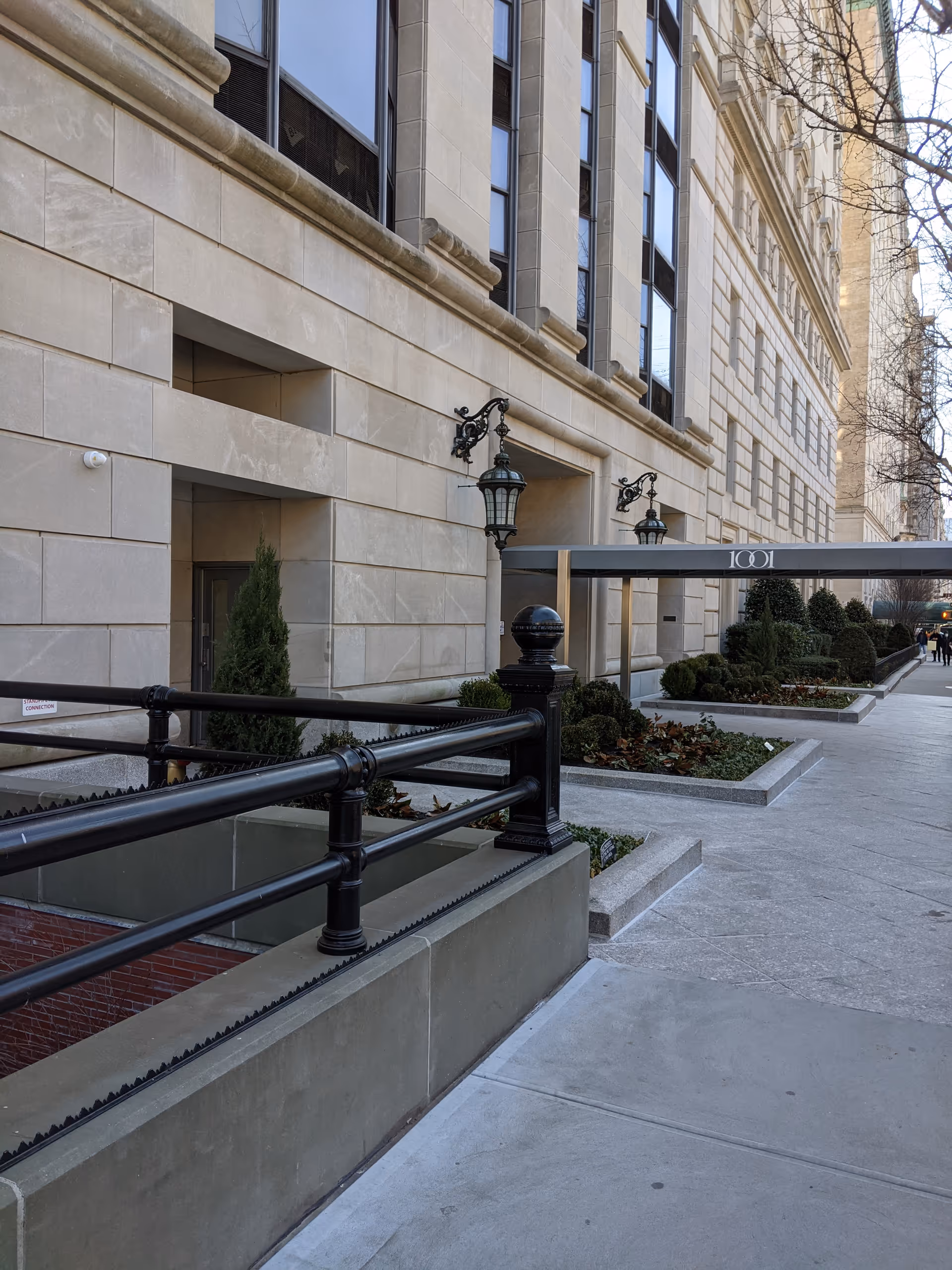 Stone building exterior with entrance canopy, decorative lamps, and landscaped walkway.