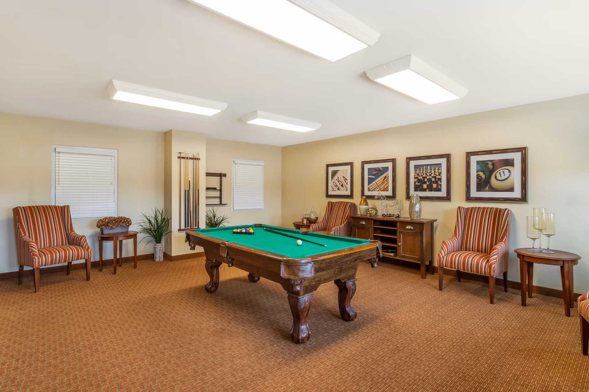 Recreation room featuring a billiards table, striped armchairs, and framed wall art.