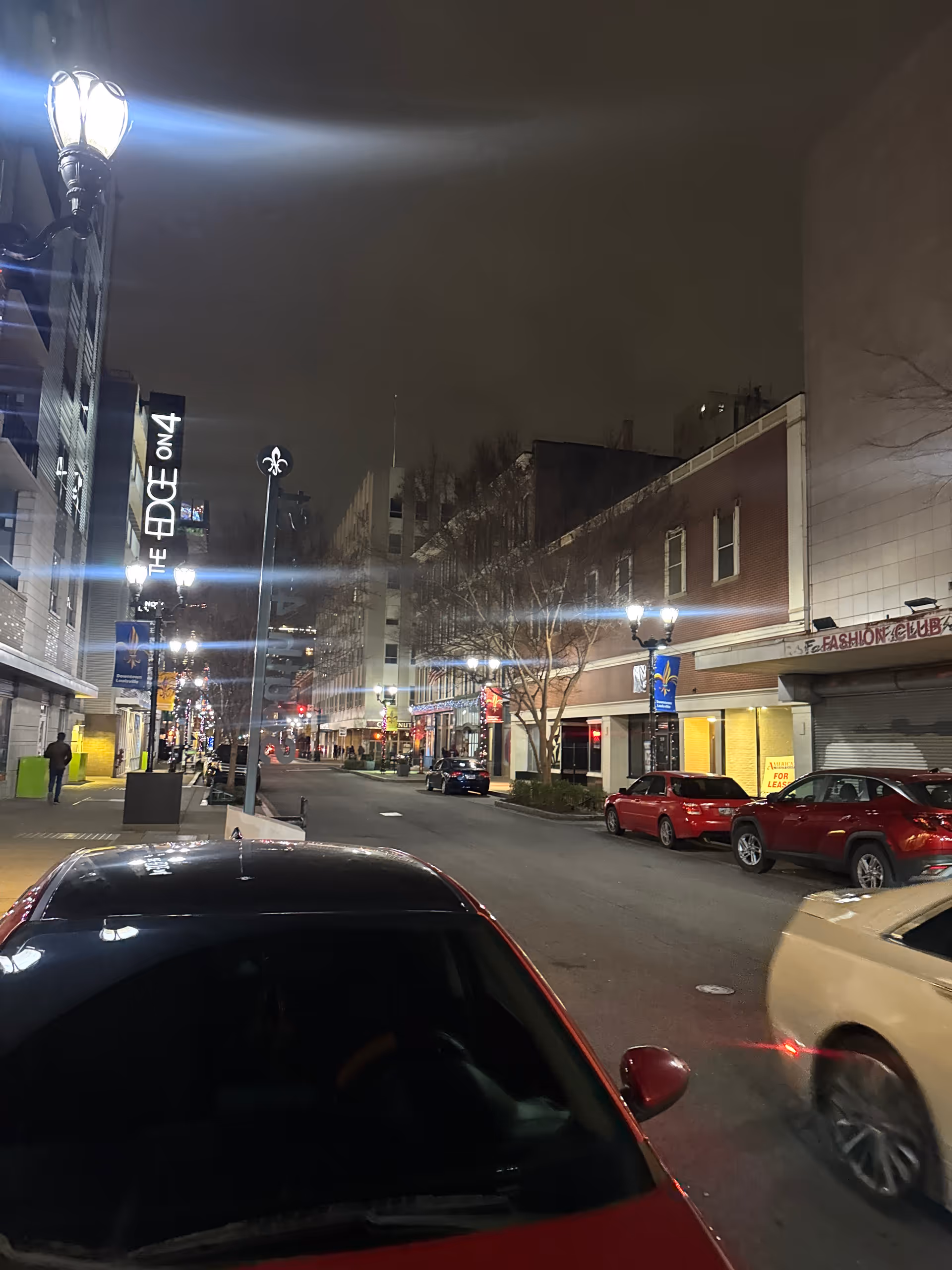 Night street view with storefronts and parked cars along a quiet downtown block.