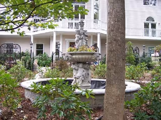 Outdoor courtyard with a stone fountain, greenery, and a white multi-story senior residence.