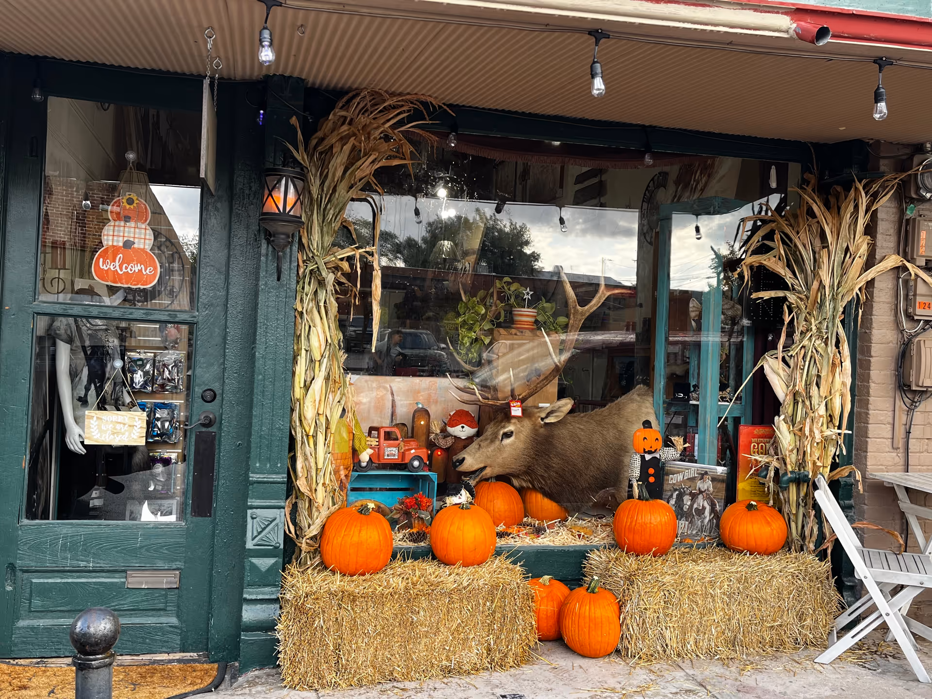 Storefront facade with autumn pumpkins, hay bales, and cornstalks in display.