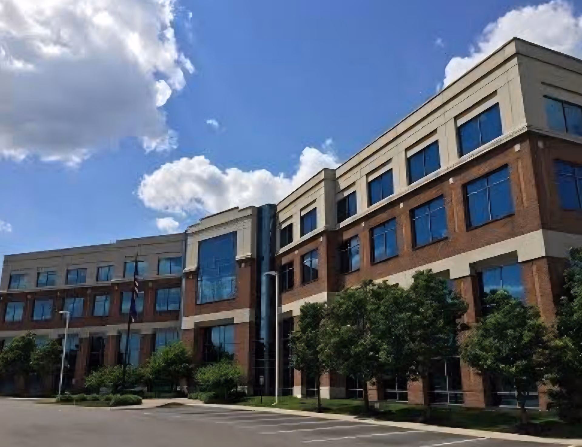 Multi-story brick senior living building with large windows and trees under blue sky.