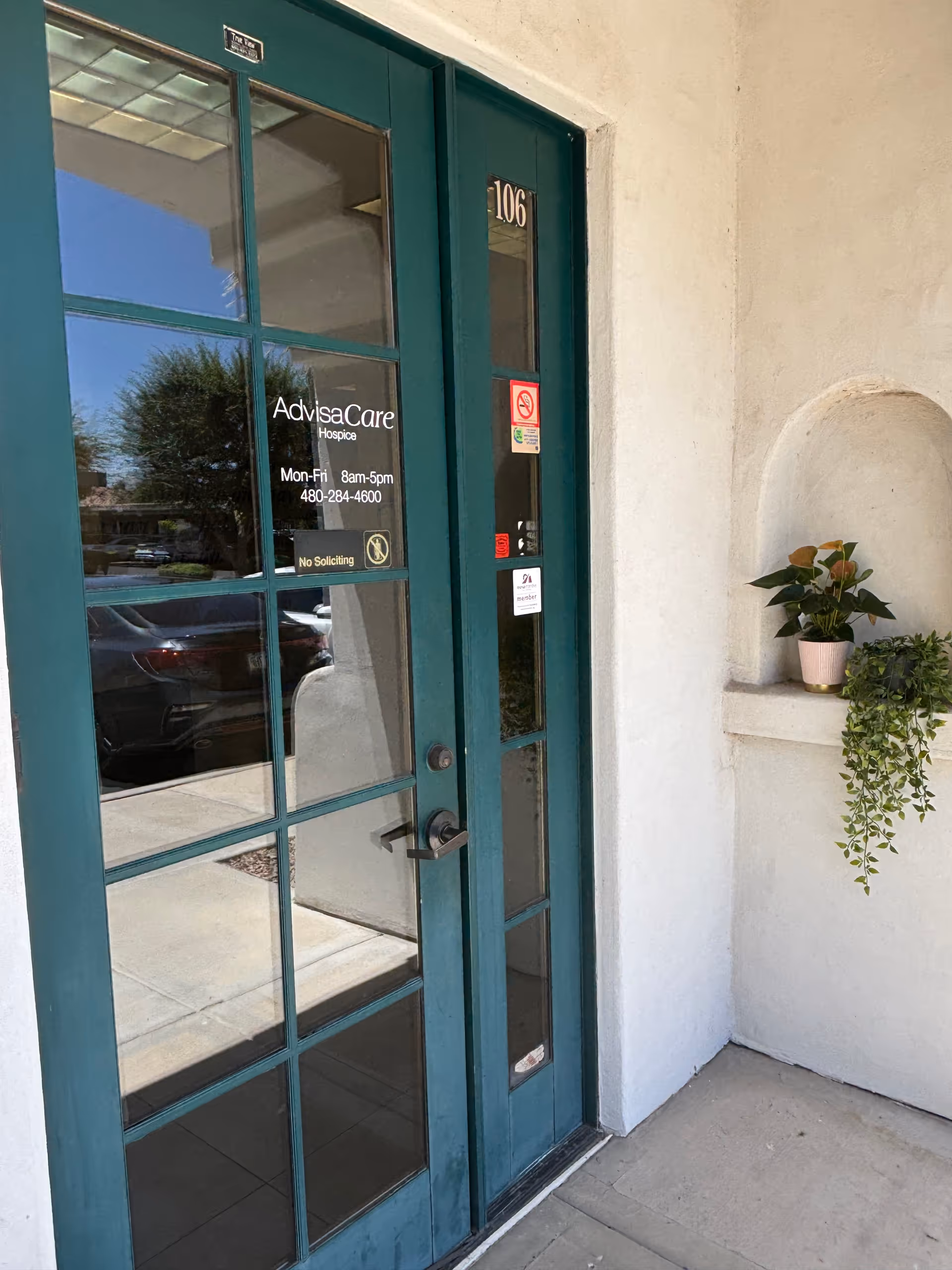 Teal-framed glass entrance door with AdvisaCare signage and a potted plant.
