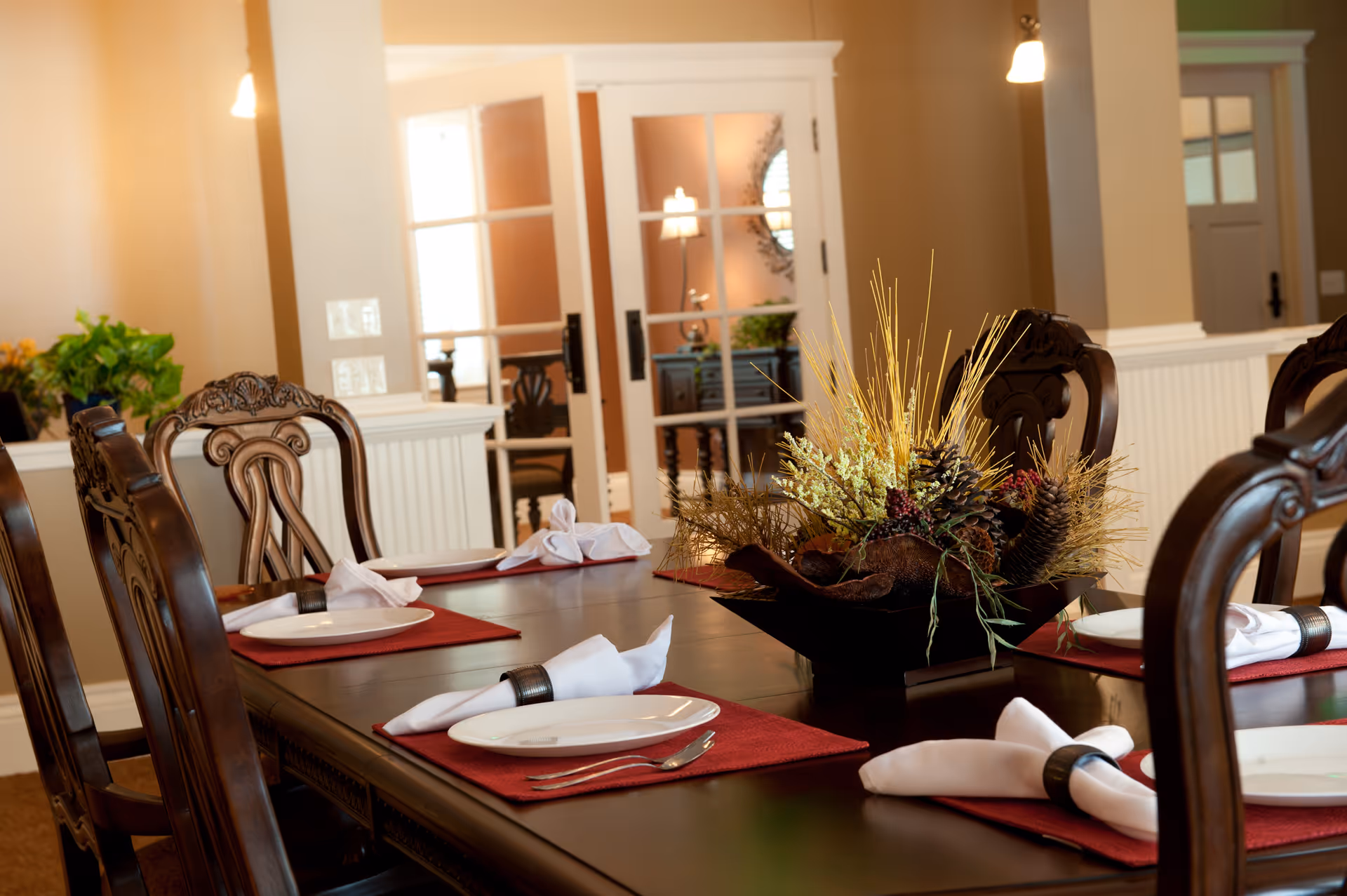 Elegant dining room with a large table, red placemats, white napkins, and floral centerpiece.