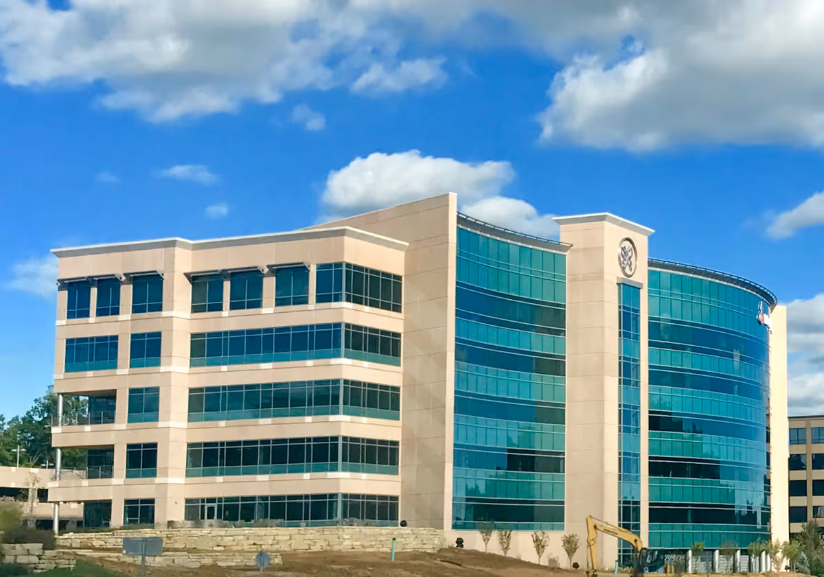 Modern multi-story building with curved glass facade under a bright blue sky.