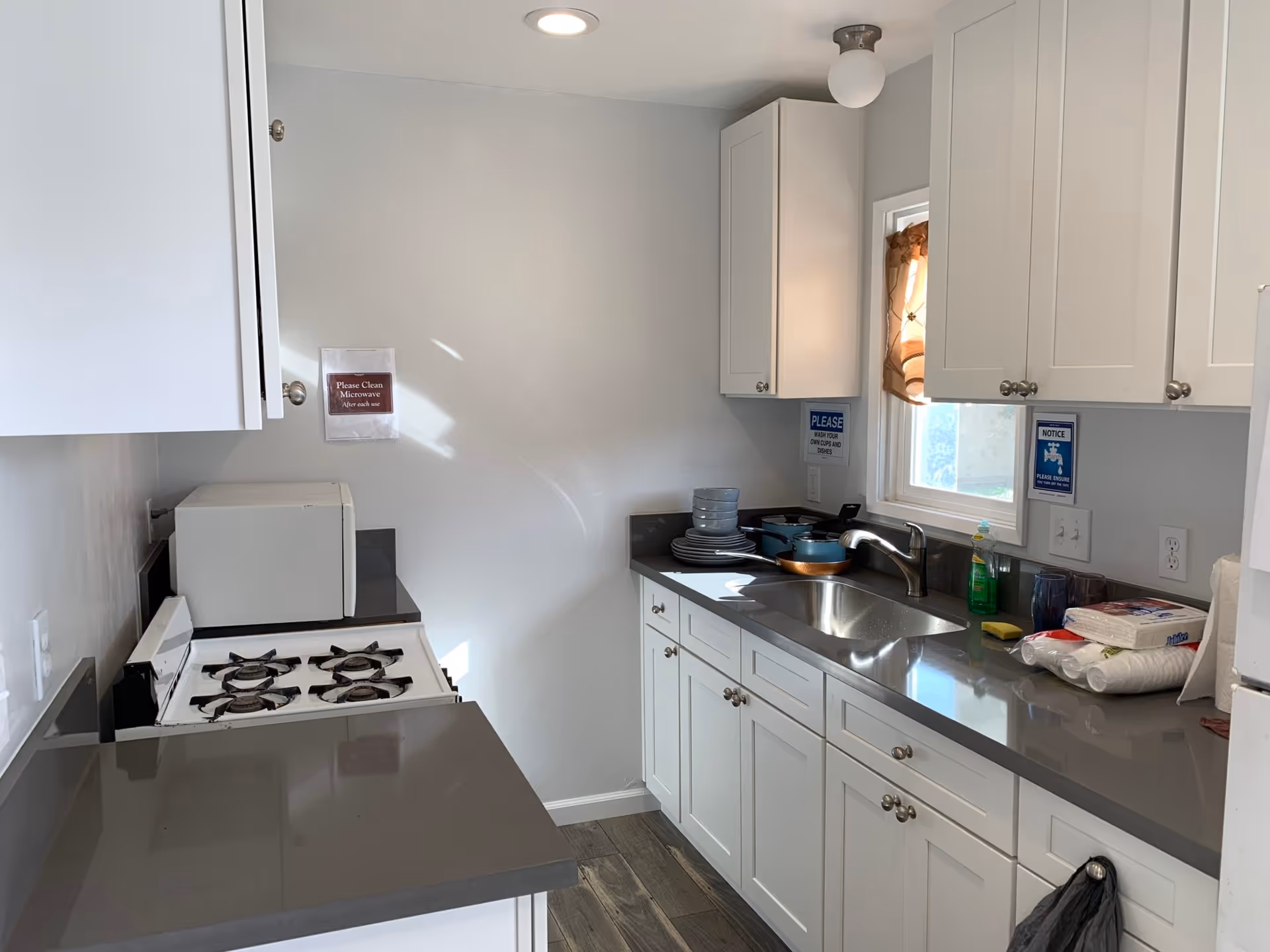 Compact kitchen with white cabinets, gray countertops, a stove, microwave, and sink.