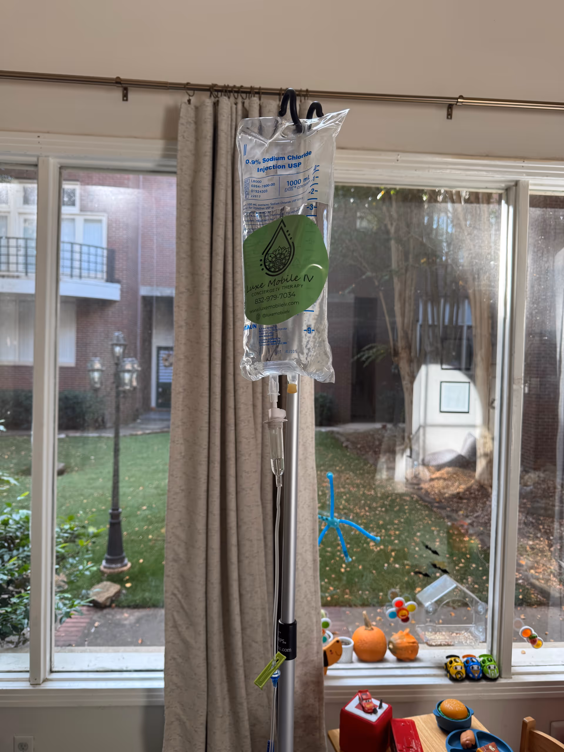 IV infusion bag on a stand inside a living room by a window.