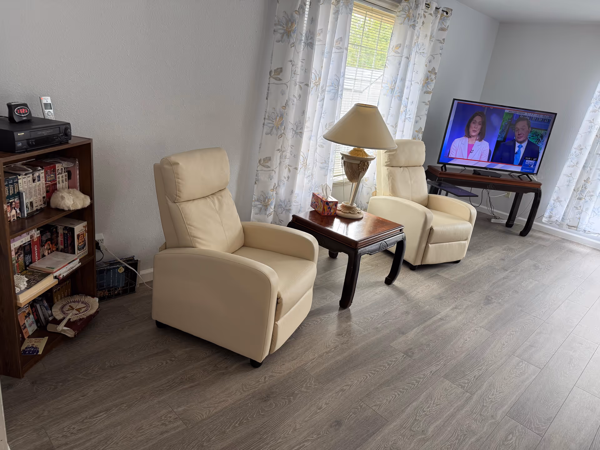 Two beige recliners, a wooden side table, and a TV in a bright living room.