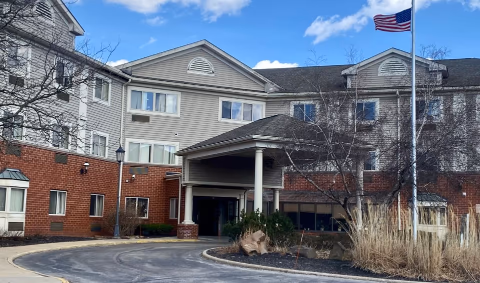Exterior view of Hospitality House Inc, a senior living facility with brick base and entrance canopy.