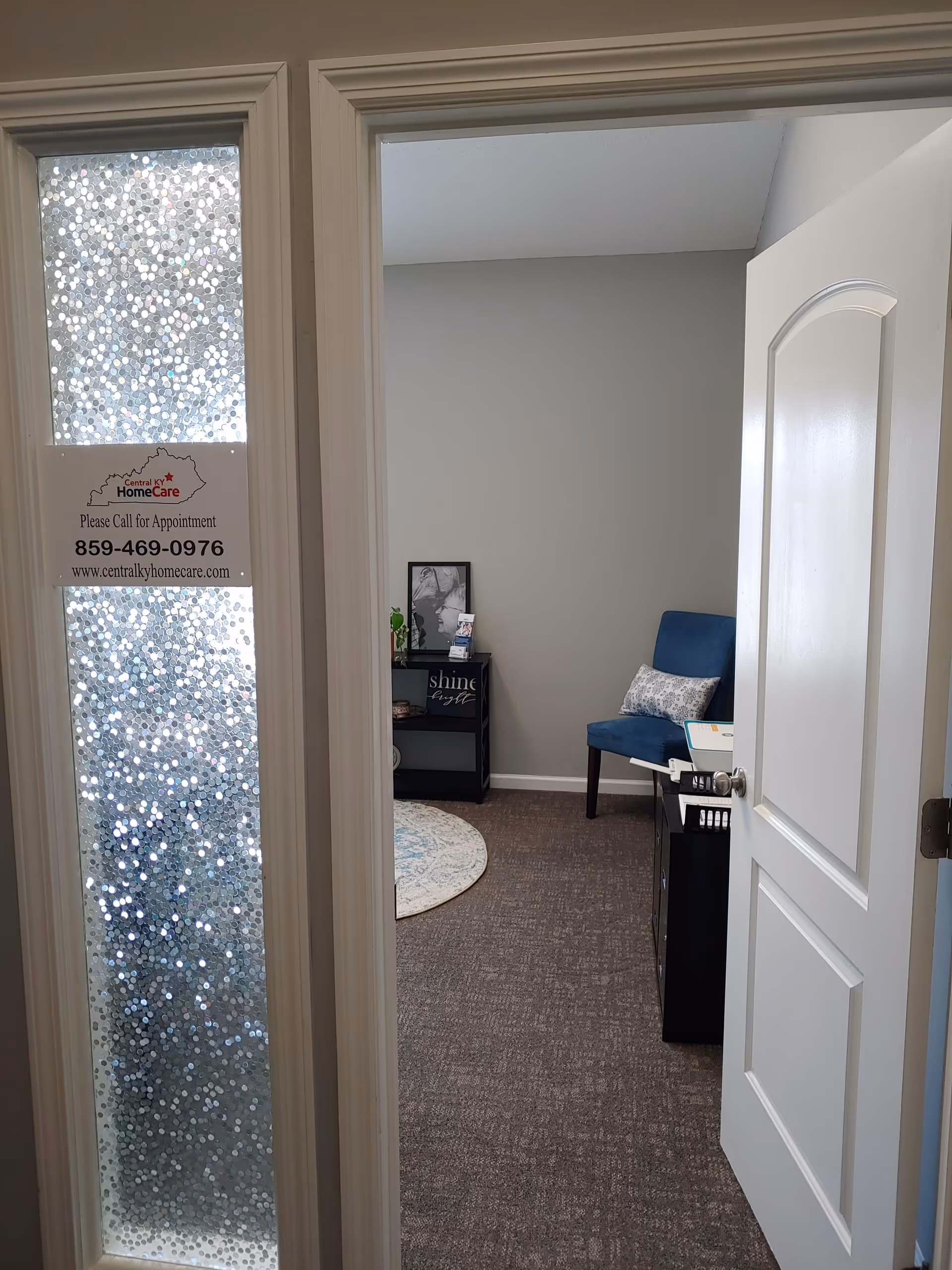 Doorway opens to a small, furnished office area with a blue chair and informational sign.