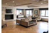 Spacious senior living lounge with beige sofa, chairs, fireplace, and large windows.