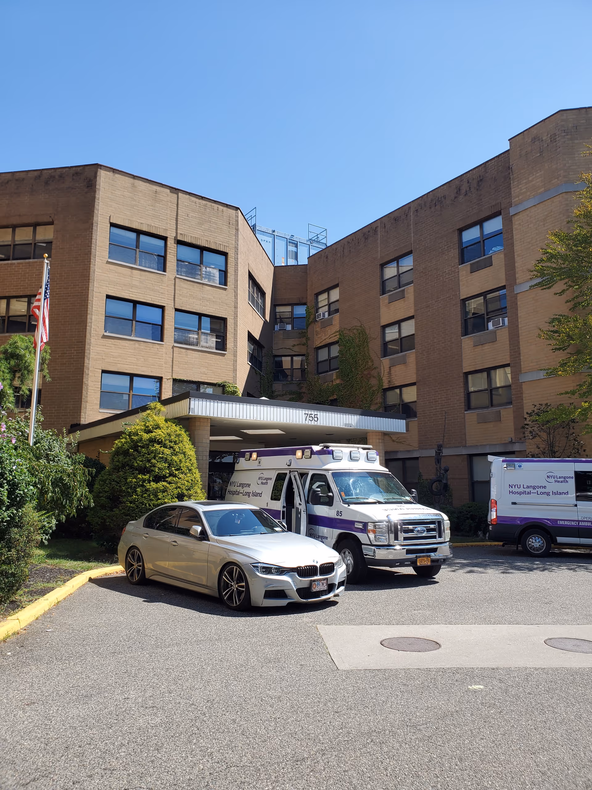 Beige brick building exterior with a covered entrance and parked ambulances.