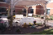 Outdoor courtyard at Southington Care Center with wooden pergola, white benches, and potted plants.