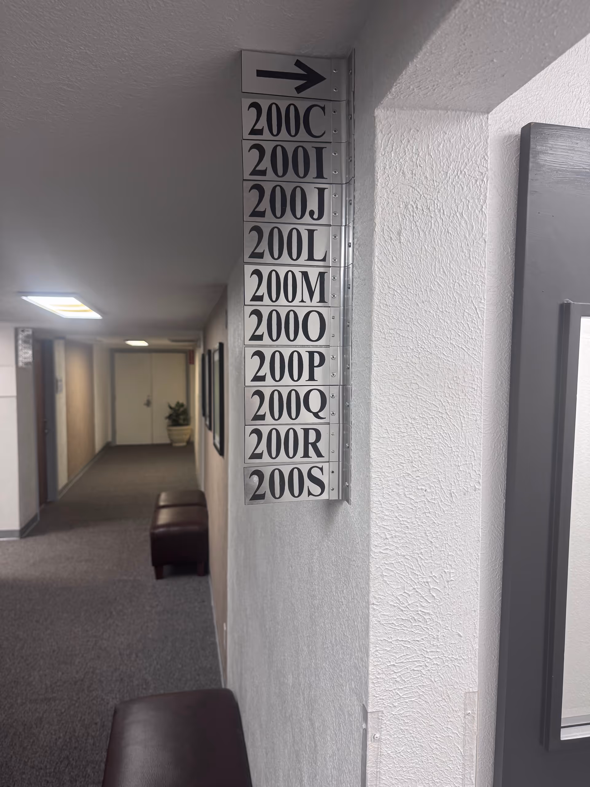 Interior hallway in a senior living facility with a vertical room-number sign and seating.