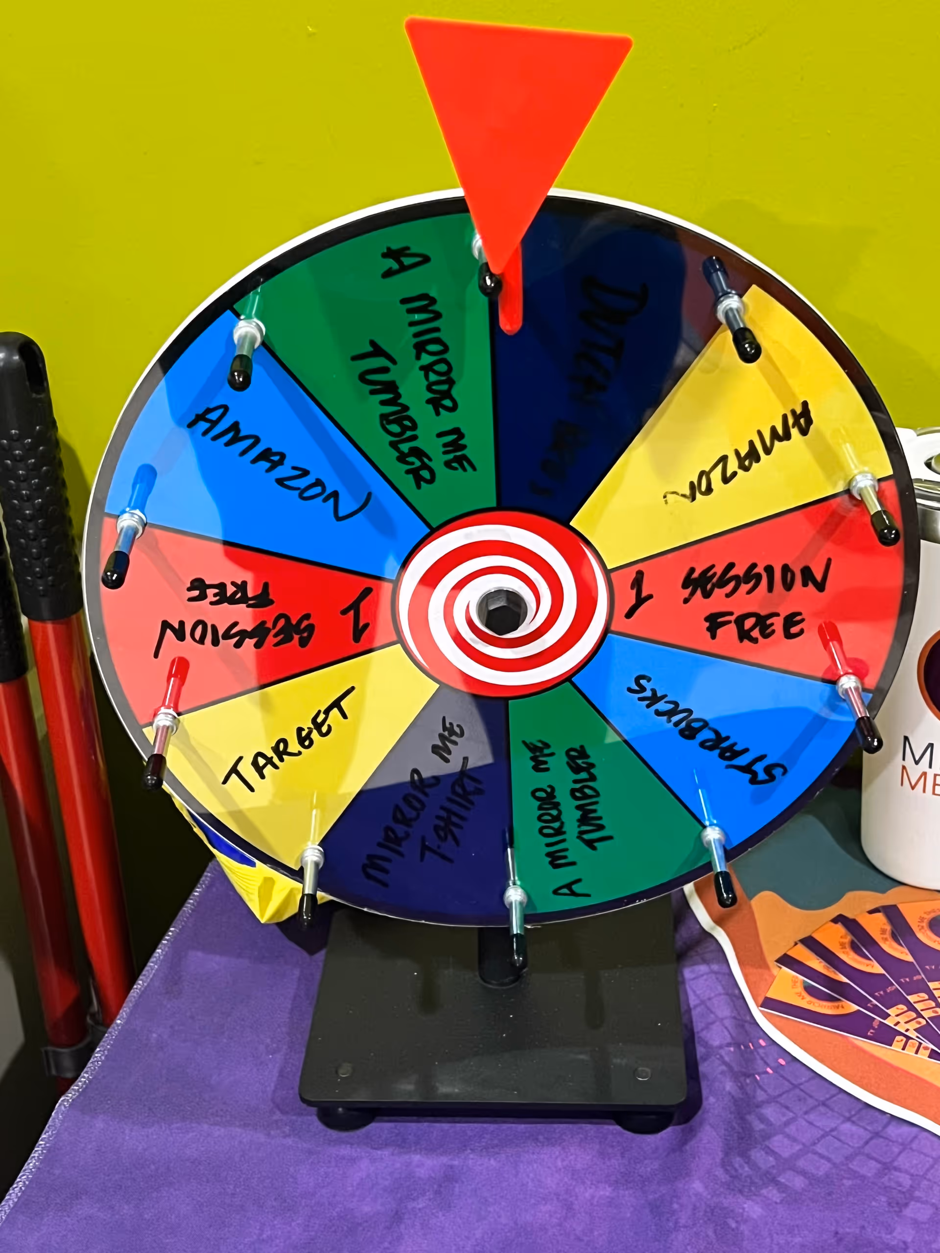Colorful spinning wheel game on a table inside a facility, with a Mirror Me Therapy mug.