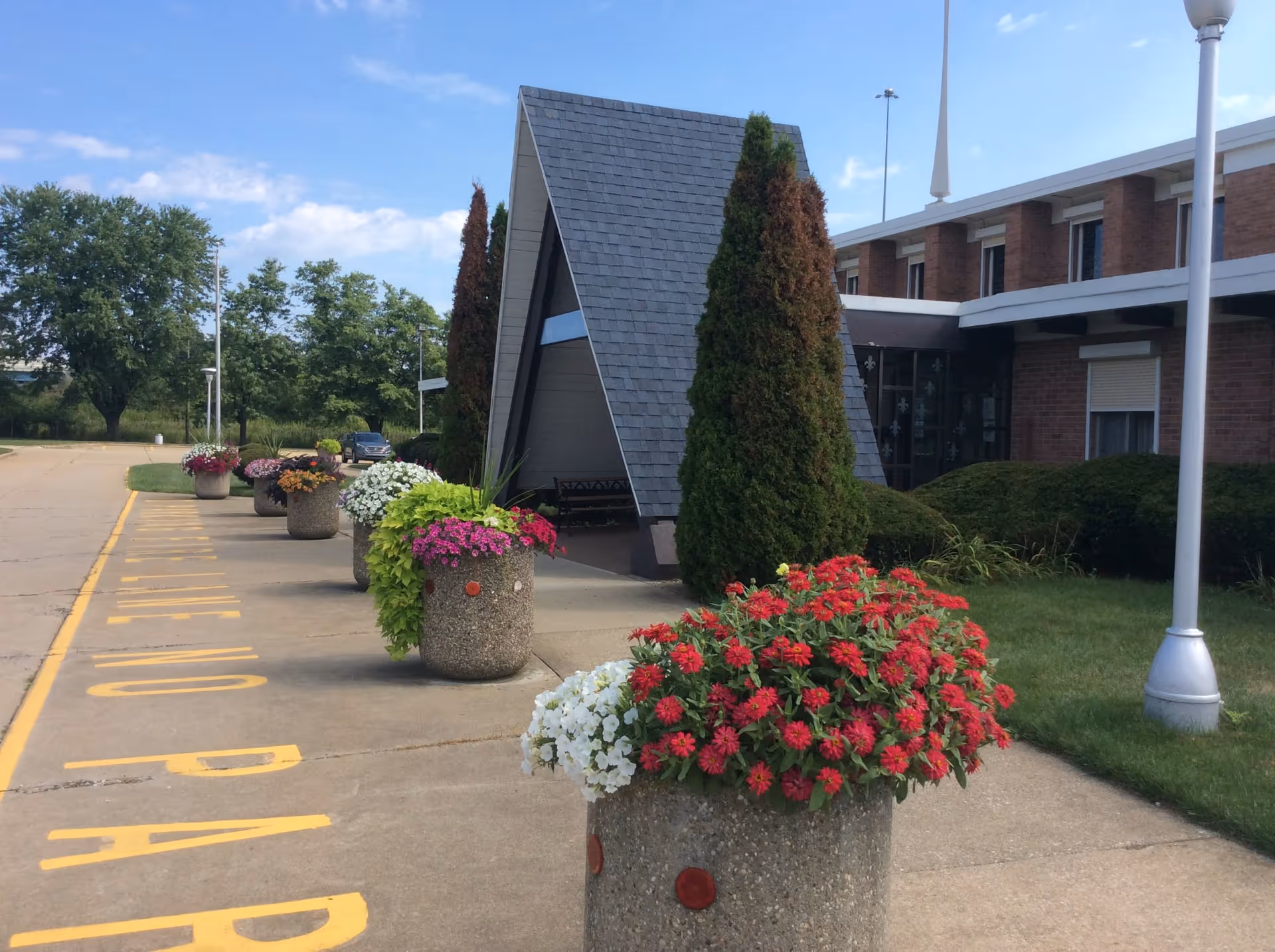 Exterior view of House of Loreto with brick building, landscaping, and flower planters along walkway.