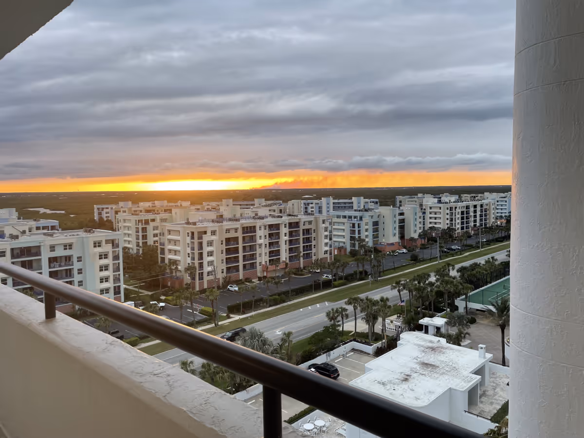 Sunset over a row of white apartment buildings viewed from a balcony with palm trees
