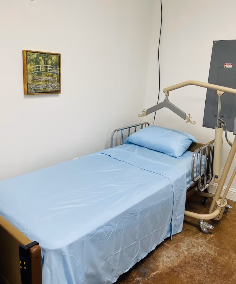 Small bedroom in a care facility with a hospital bed and ceiling lift.