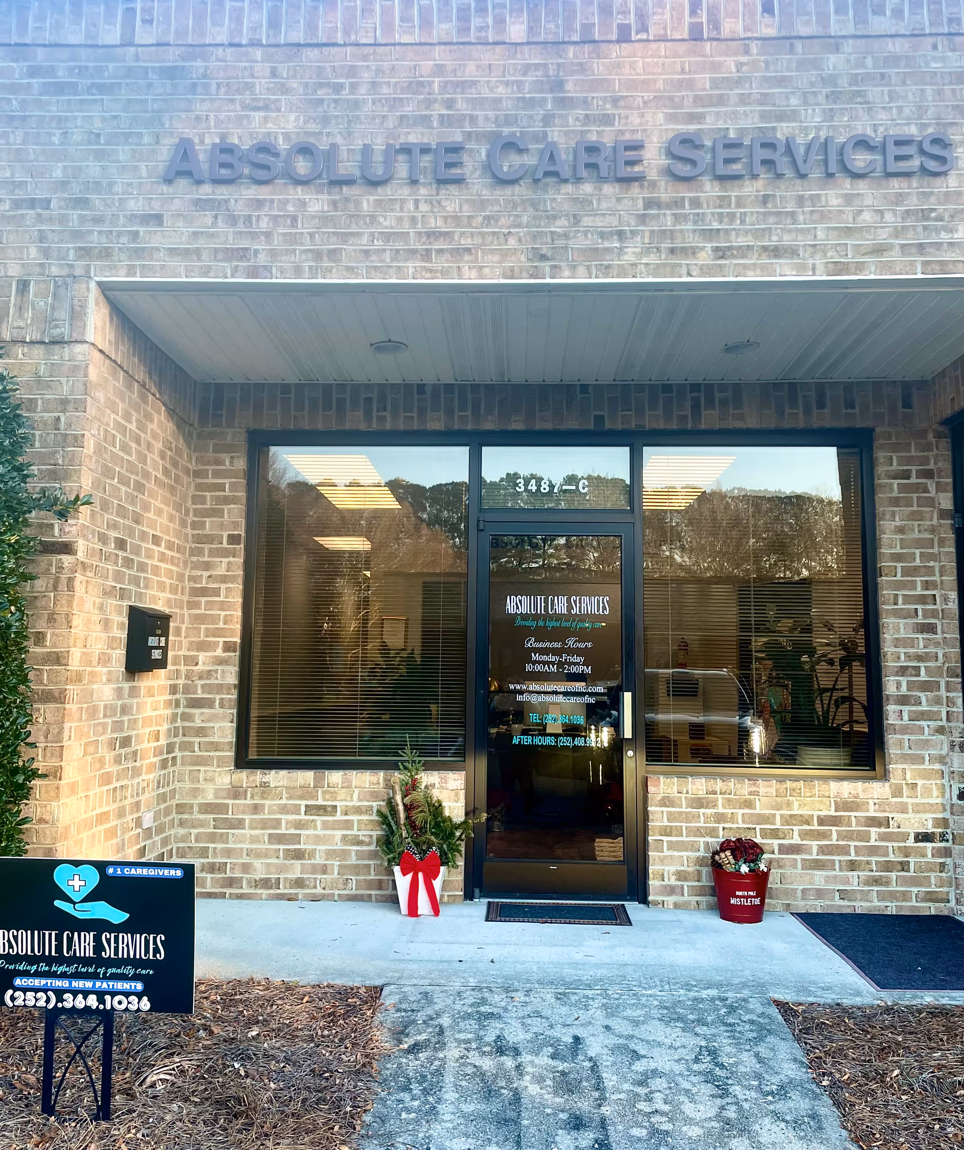 Front exterior of Absolute Care Services building with glass entrance and potted plants.