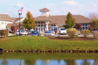 Exterior view of The Addison of Park Crescent with parked cars and a pond.
