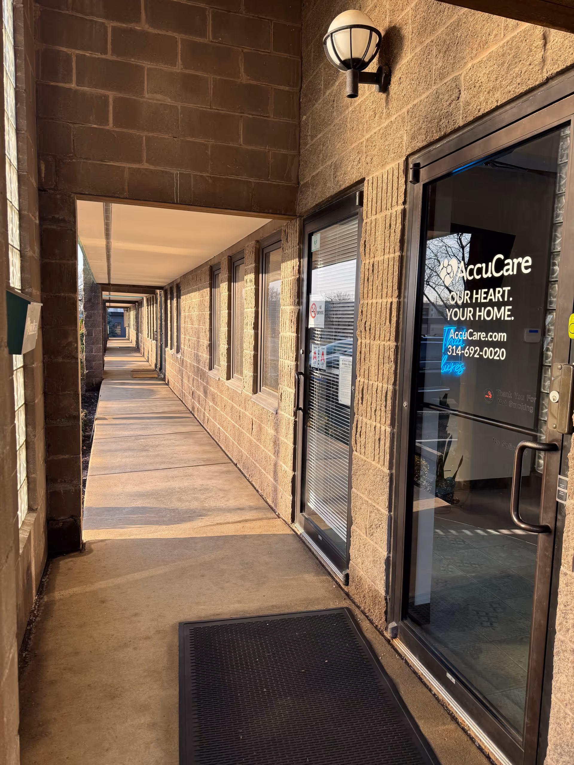 Exterior hallway along AccuCare facility with glass entrance door and brick walls.