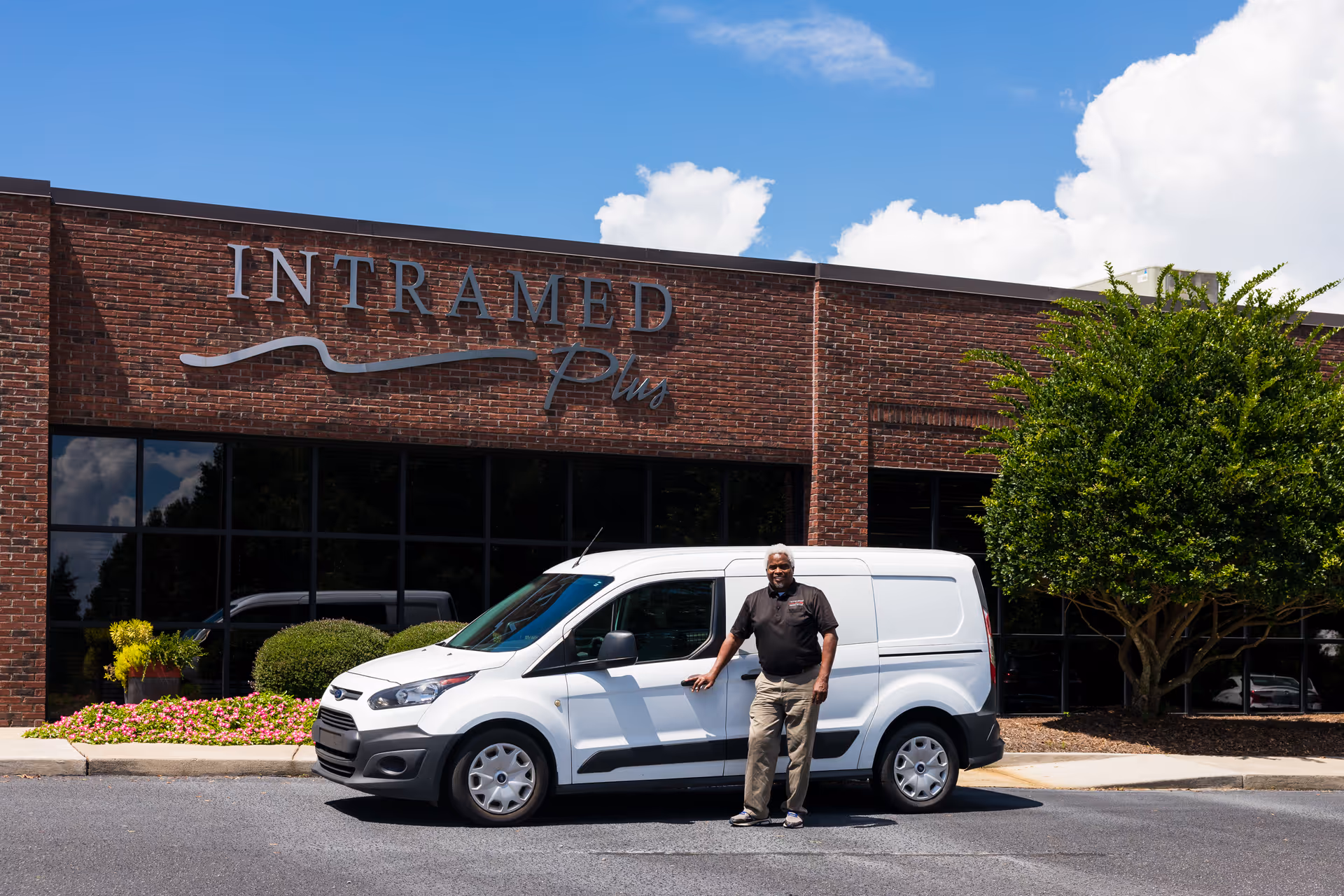 A man stands beside a white van in front of Intramed Plus facility.