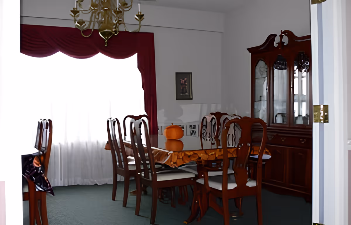 Formal dining room with a wooden table and chairs, china cabinet, chandelier, and a curtained window.