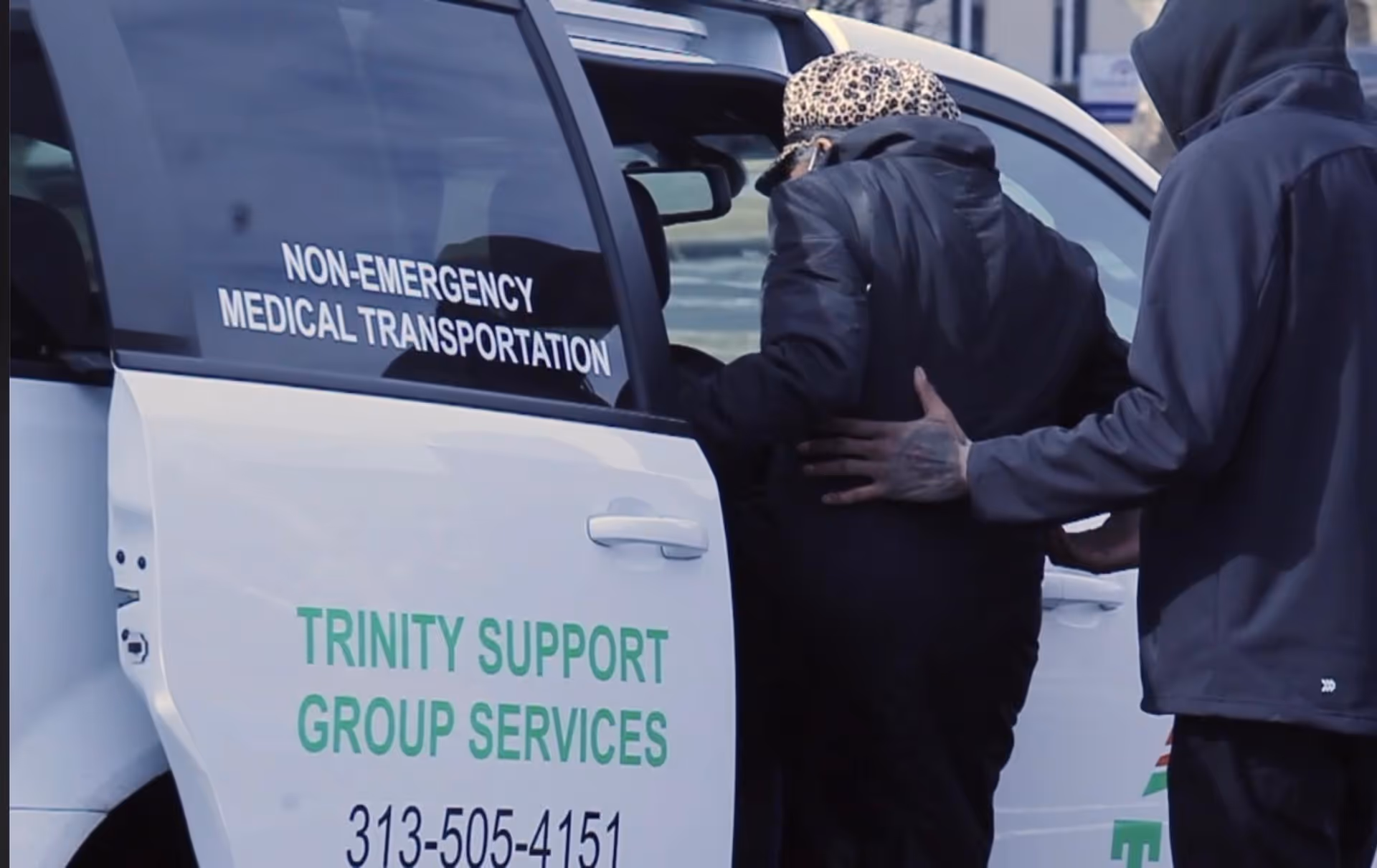 Exterior view of a white service van labeled Trinity Support Group Services with two people nearby.