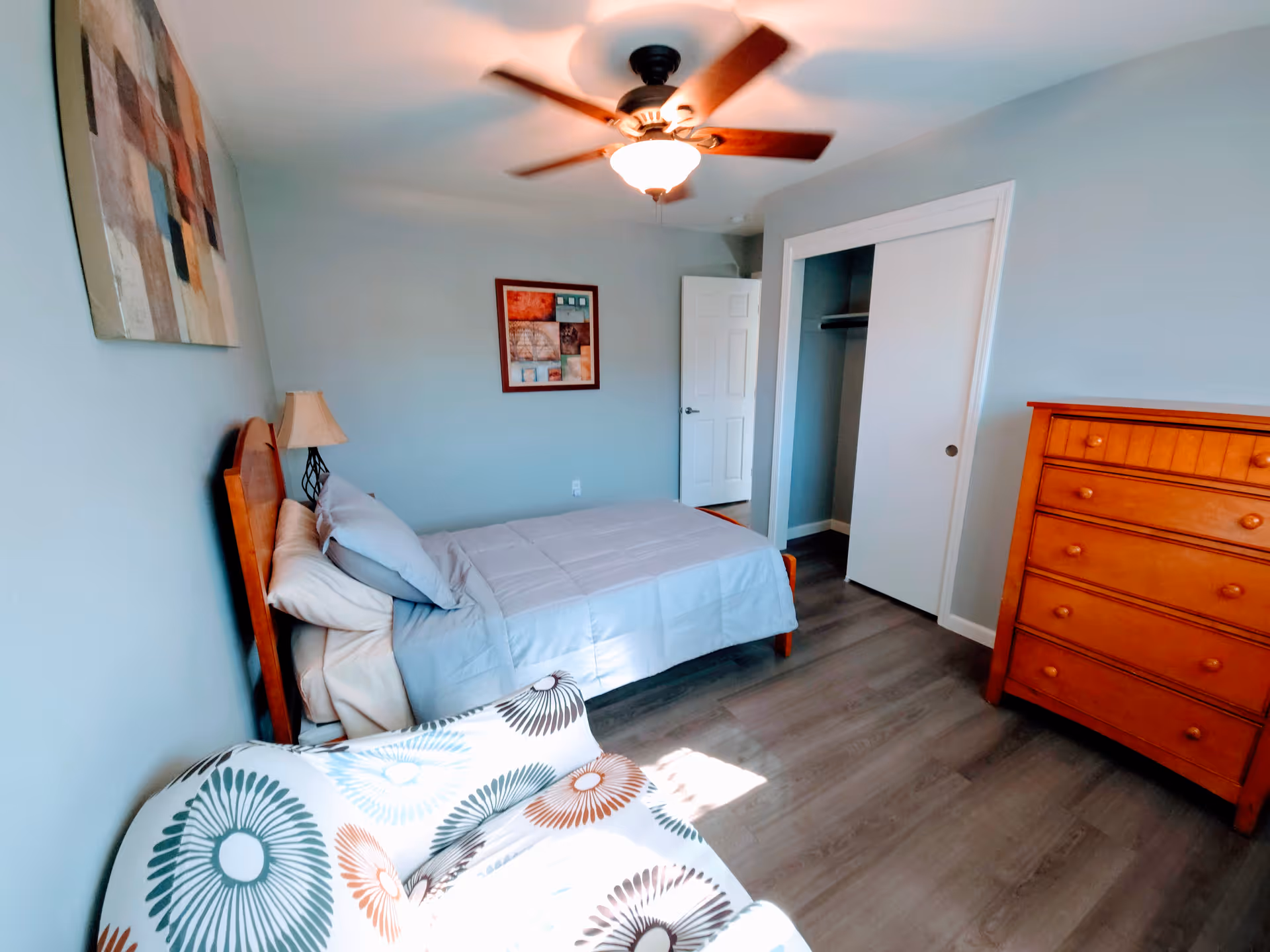 Blue bedroom with a wooden bed, dresser, chair, and ceiling fan.