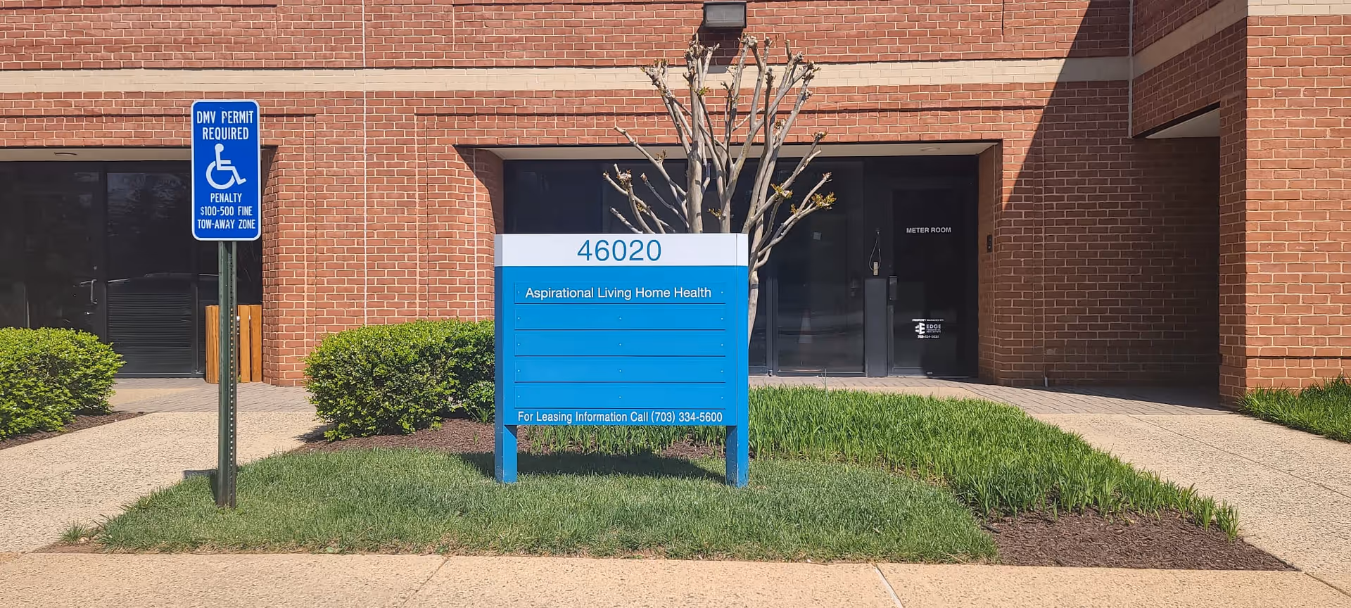 Brick building entrance with blue address sign and neatly trimmed shrubs in front