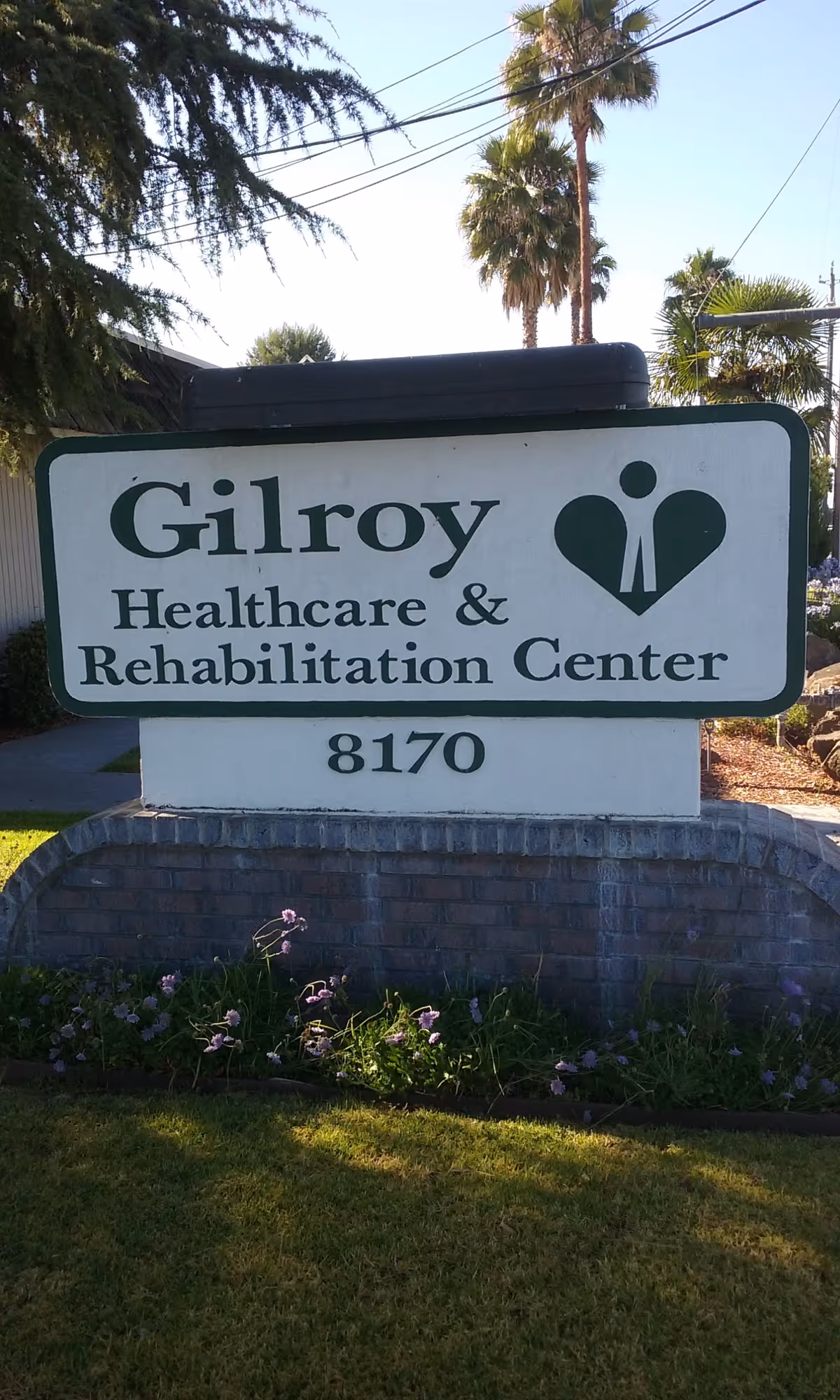 Exterior sign for Gilroy Healthcare & Rehabilitation Center on a brick pedestal with palm trees