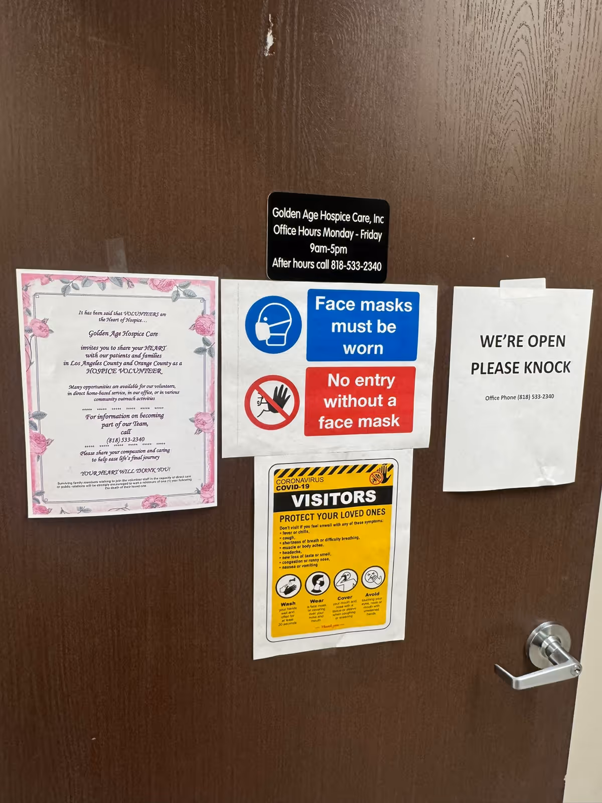 Wooden interior door crowded with notices about masks and visiting hours.