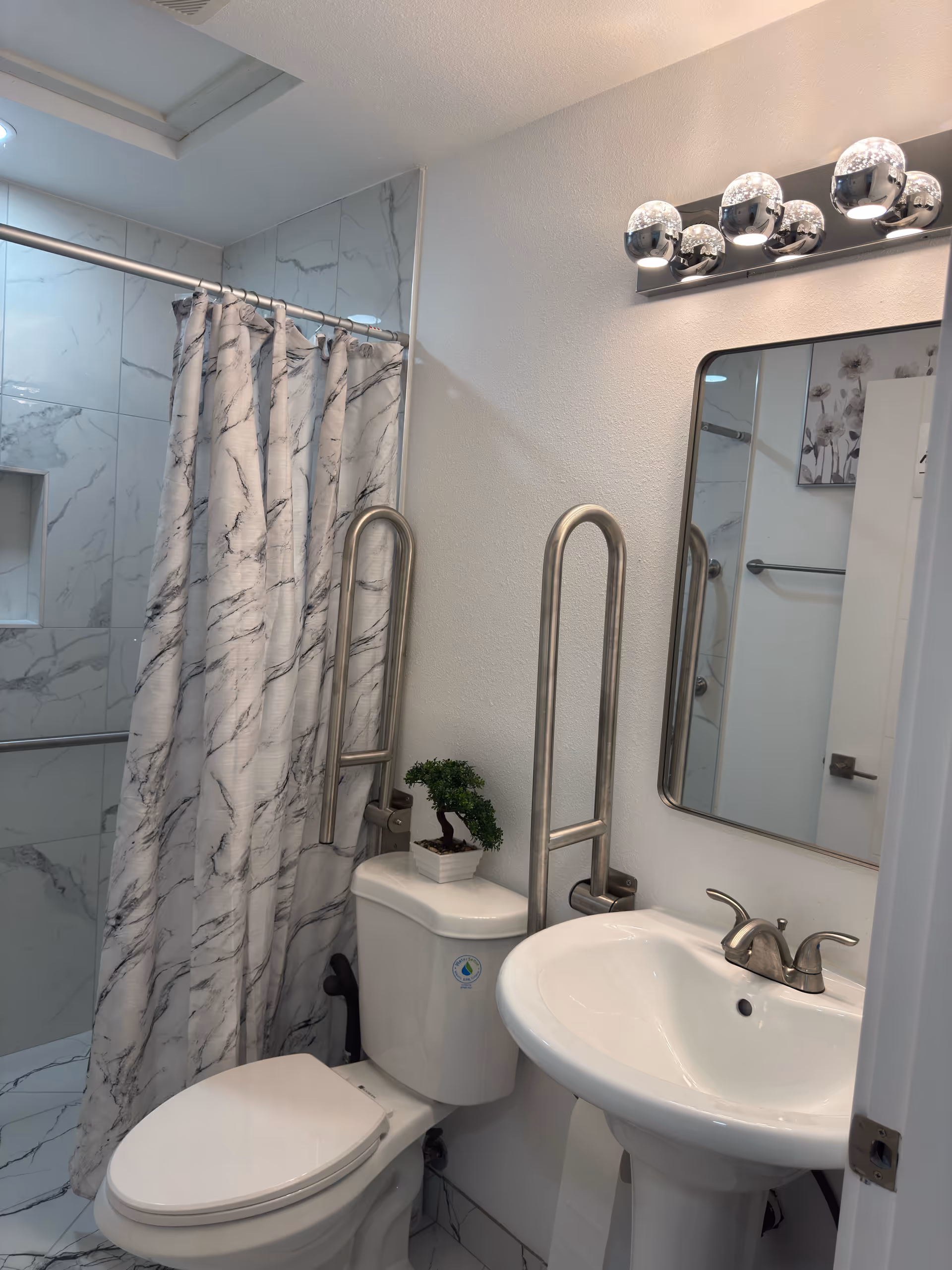 Accessible bathroom featuring toilet, pedestal sink, mirror, shower with curtain, and grab bars.