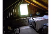 Rustic attic bedroom with metal-framed bed, quilt, wooden walls, and a bright window.