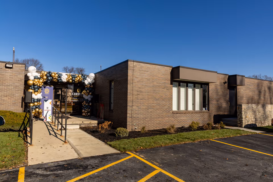 Exterior view of a brick Cherish Hospice entrance with balloon arch and parking.