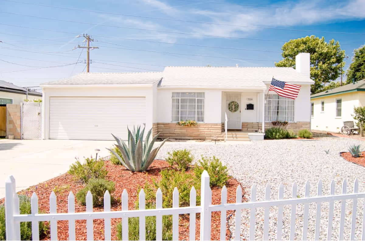White, single-story building with a two-car garage, front yard, and American flag.