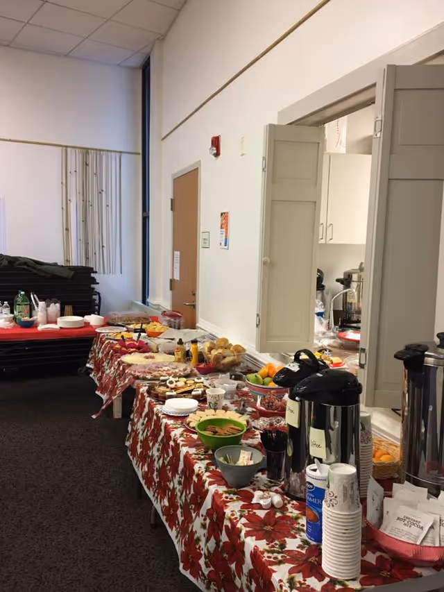 A long buffet table with assorted foods and coffee in a bright interior room.