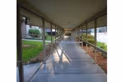 Covered outdoor walkway with railings, a concrete path, and lawns beside a building.