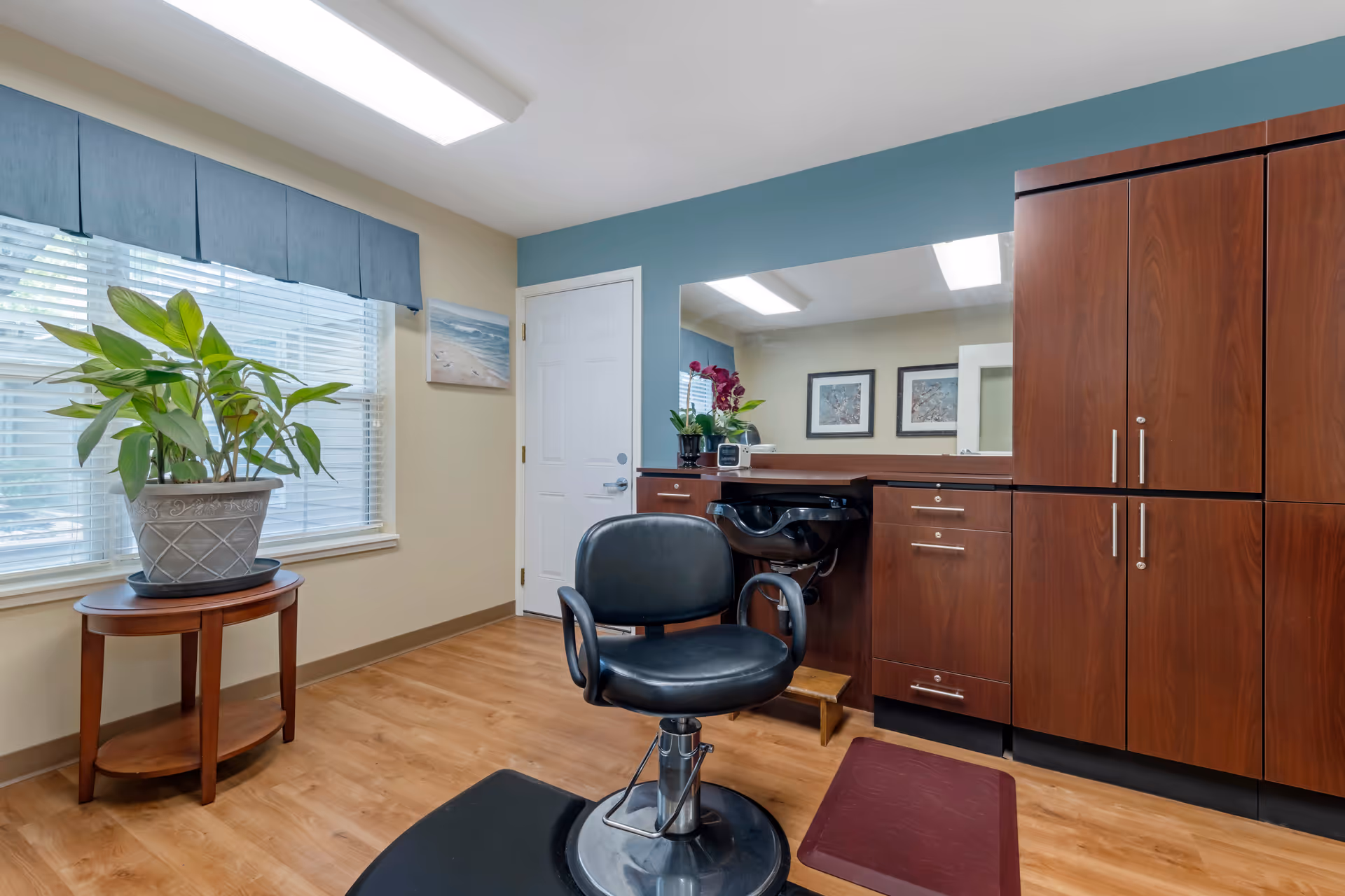 Interior room in a senior living facility featuring a barber chair, cabinets, mirror, and plant.