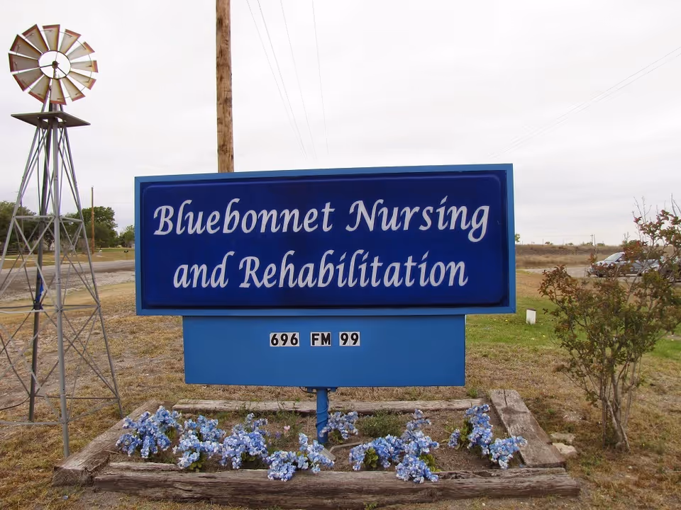 Bluebonnet Nursing and Rehabilitation sign with a windmill and flowers in a rural lot.