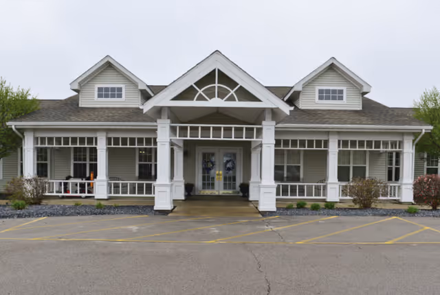 Front entrance of a single-story building with a covered porch, white columns, and double glass doors.