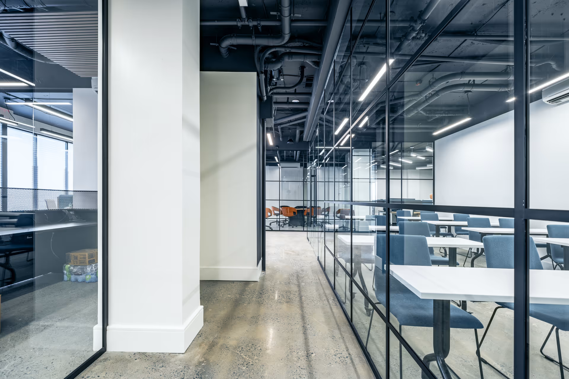 Modern glass-walled interior with white desks and blue chairs in a conference-style study area.