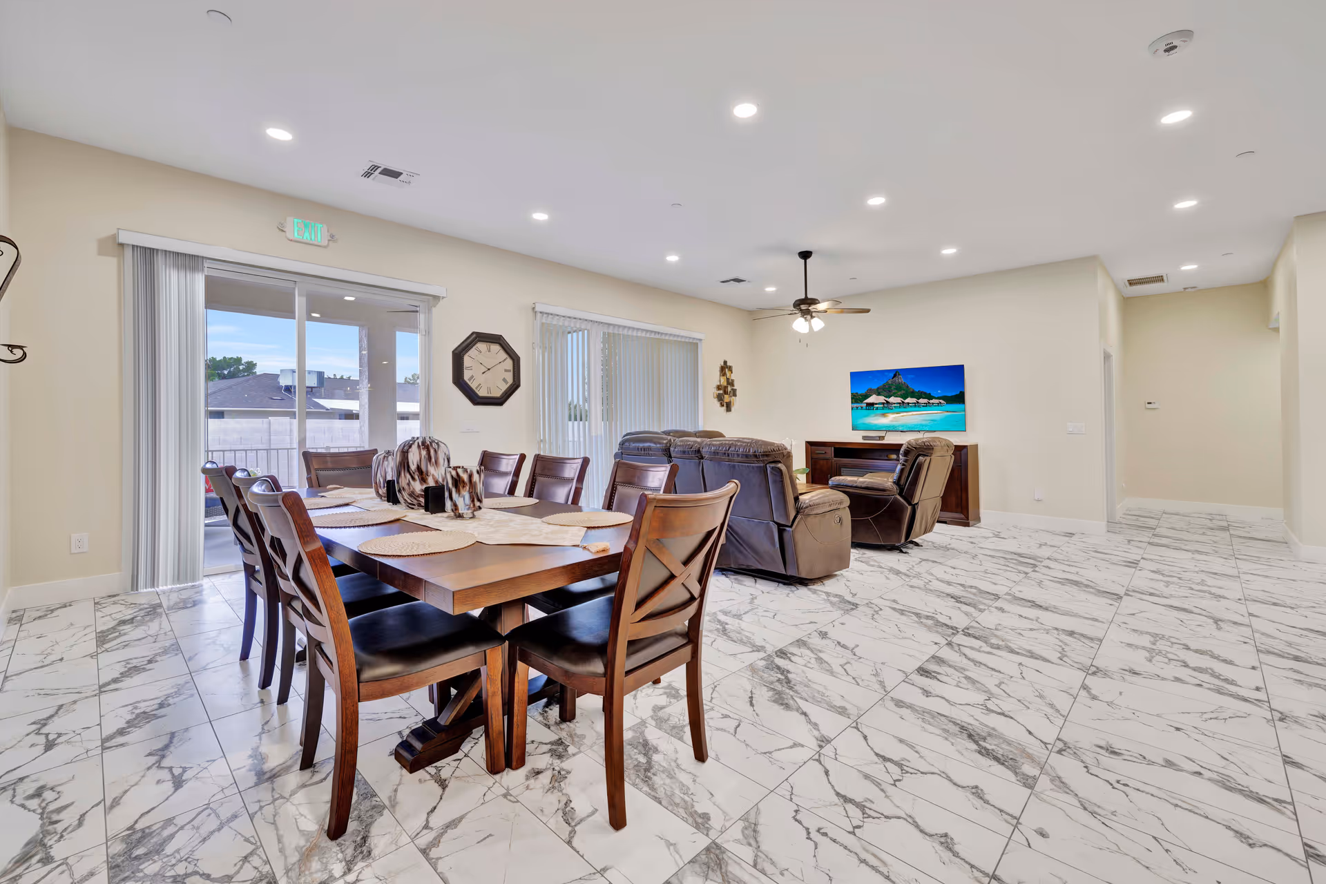 Spacious, well-lit resident dining area with a large wooden table, leather chairs, and a TV lounge.