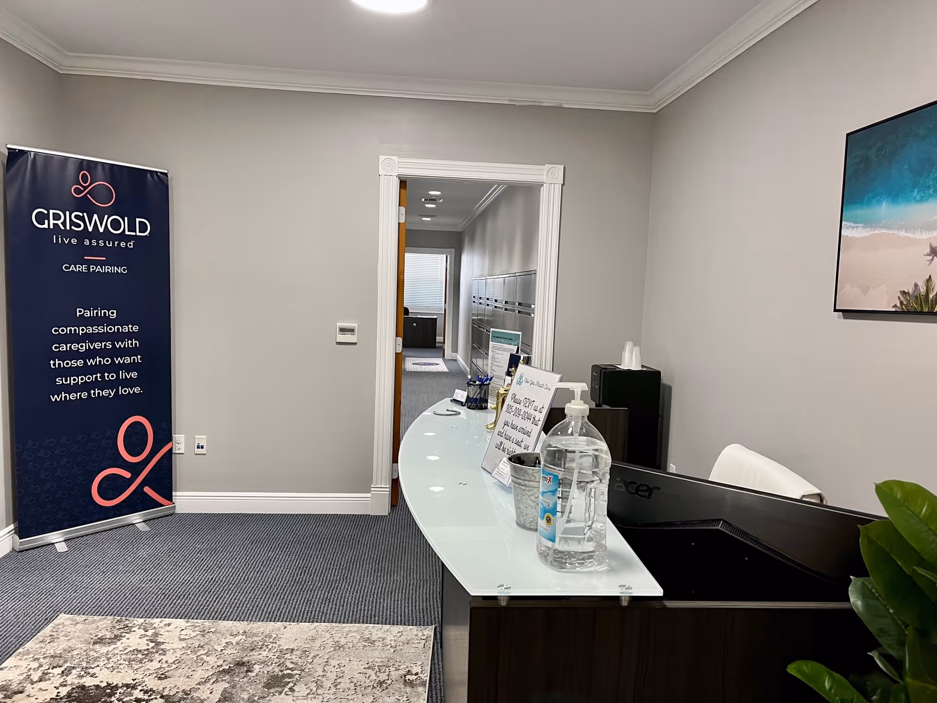 Interior reception area with curved glass desk, Griswold banner, water dispenser, and artwork.