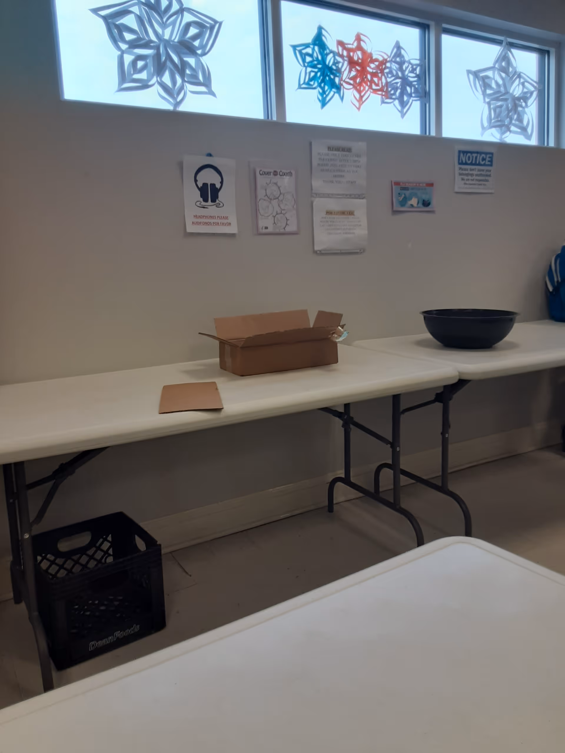 Interior room with folding tables, a cardboard box, and posted notices on the wall.