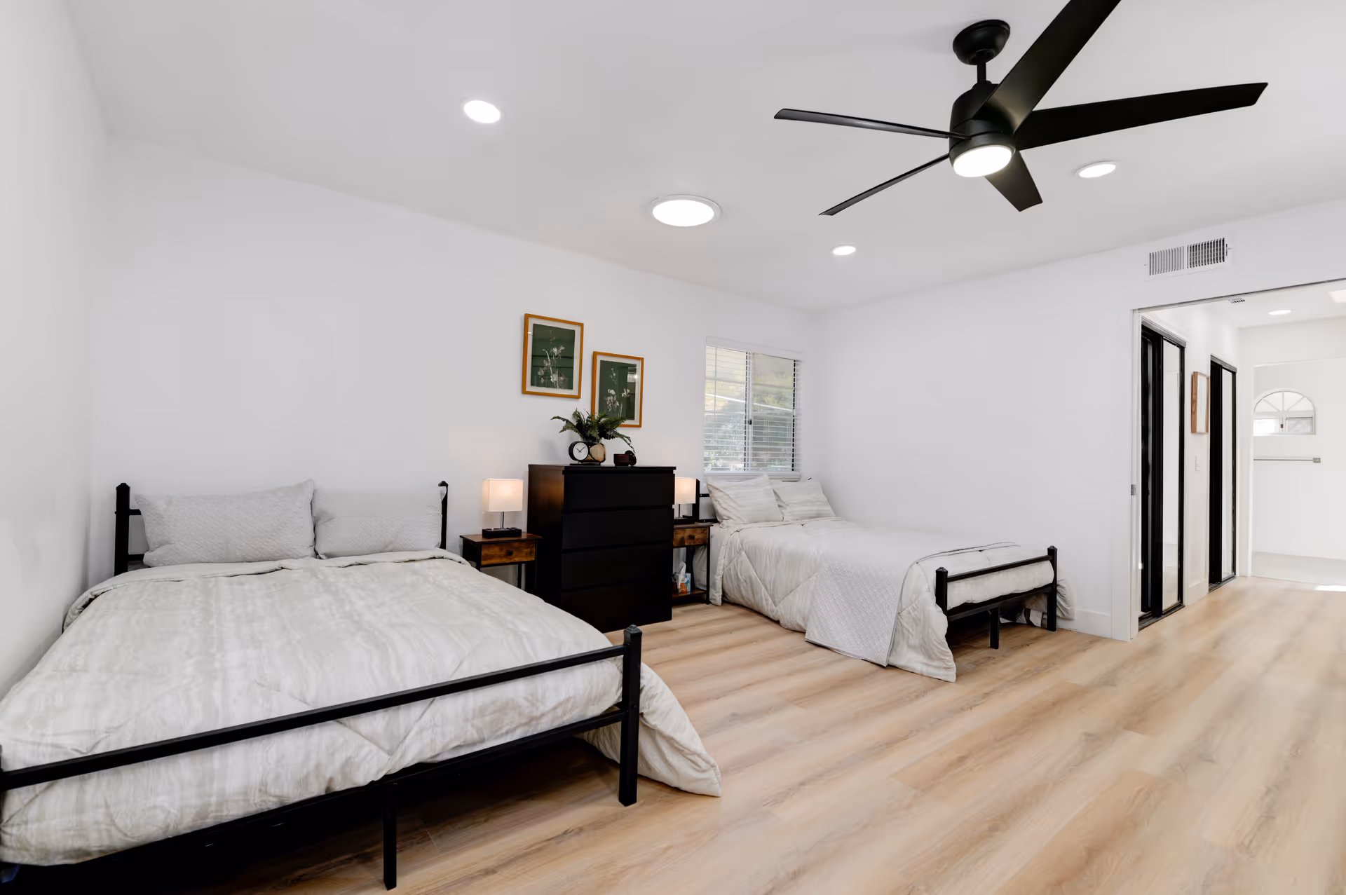 Two single beds with matching white bedding in a bright shared bedroom, wooden floor, ceiling fan.