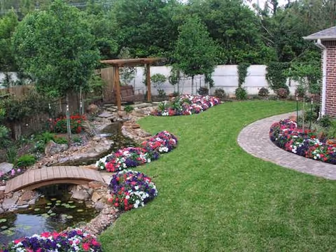 Outdoor garden with colorful flower beds, curved brick path, and a small stone bridge.
